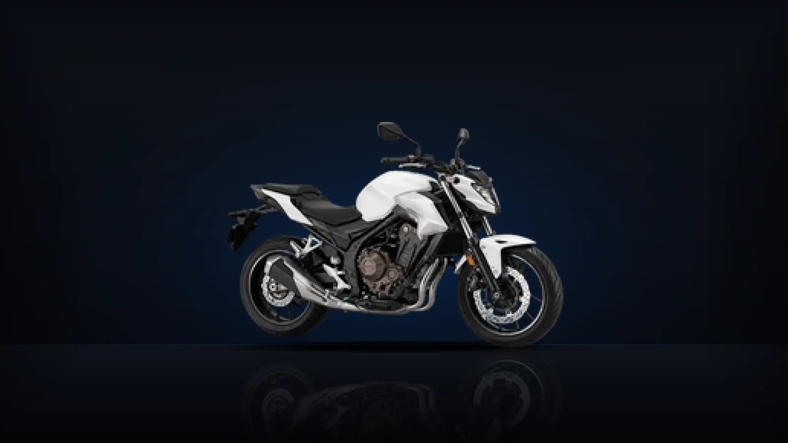 A white naked motorcycle on a dark floor showing its engine and chain drive