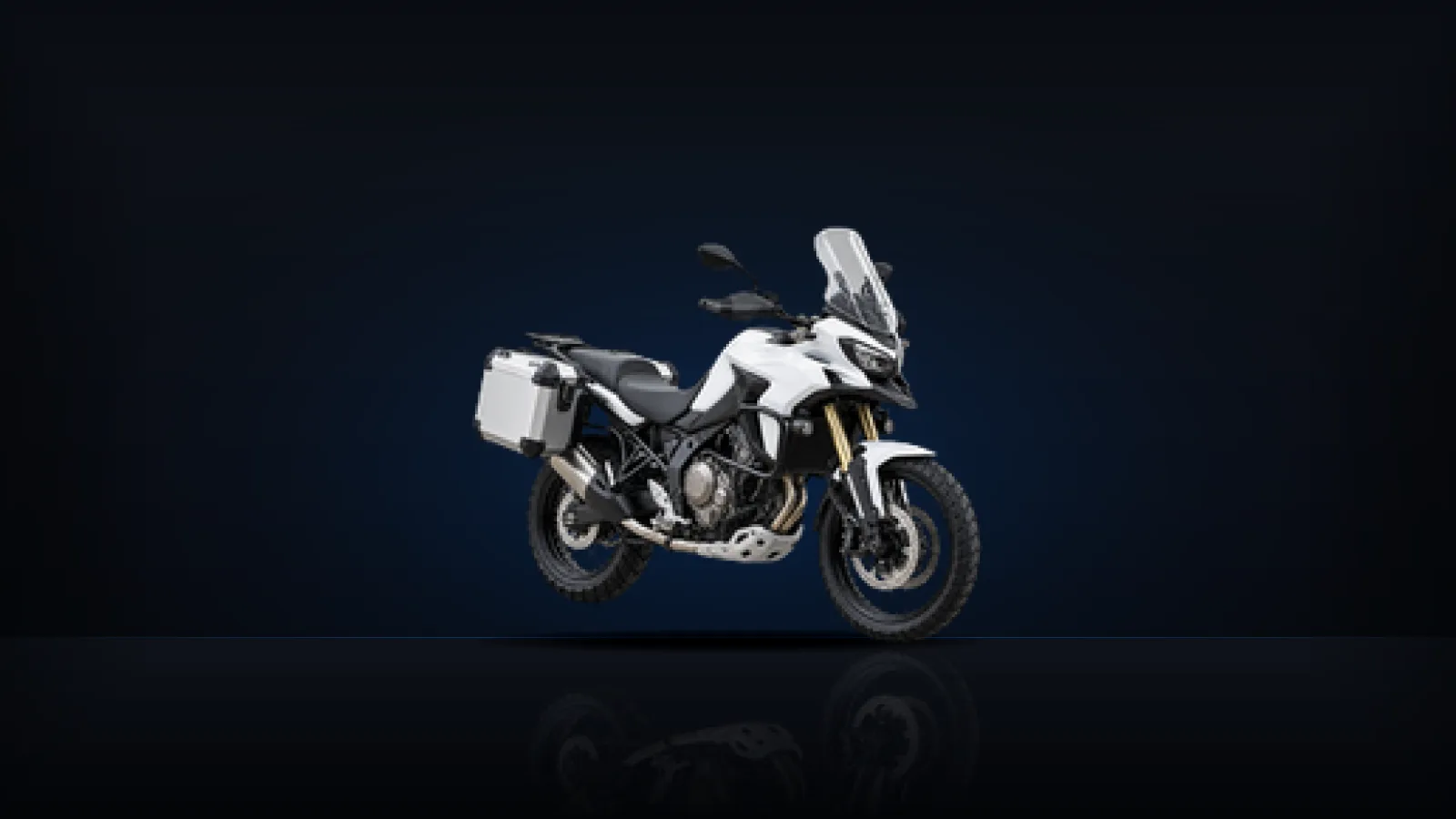 A white adventure-touring motorcycle on a dark studio floor
